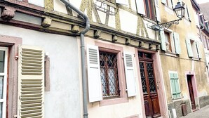 Een klassiek Europees gebouw met een puntige daktop, meerdere ramen met luiken, en een duidelijke ingang met een deur.
