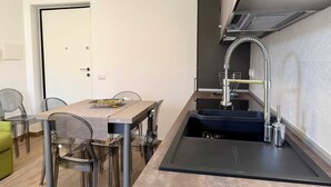 Une cuisine compacte dotée d’un évier intégré, d’une hotte en acier inoxydable et d’un coin repas avec une table et des chaises en verre.