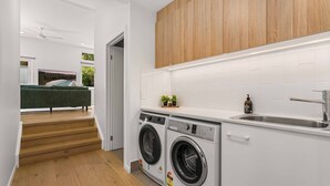A modern kitchen with white cabinetry, a built-in washing machine, and a wooden countertop. - Blenheim Breeze by Experience Jervis Bay (Vincentia)