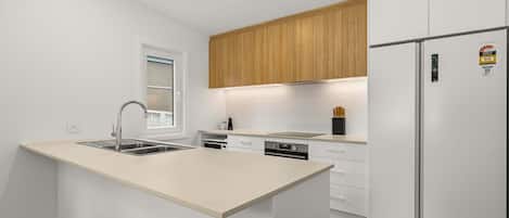 Una cocina moderna con una isla central, armarios de madera, horno empotrado y refrigerador con etiquetas de eficiencia energética.