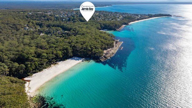 An aerial view of Jervis Bay with a beach, clear turquoise waters, and dense forested areas. - Blenheim Breeze by Experience Jervis Bay (Vincentia)