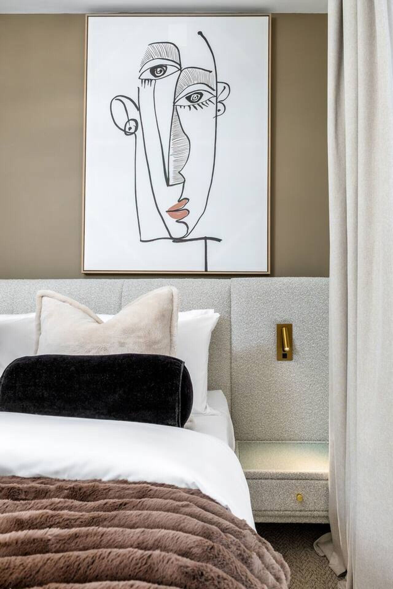 A modern bedroom with a bed, pillows, a headboard, a wall-mounted artwork, and a bedside table.