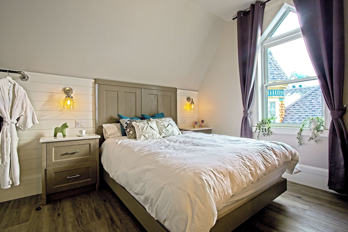 Een slaapkamer met een bed, nachtkastjes, een raam met gordijnen en een wandlamp.