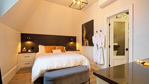 Ein Schlafzimmer mit Bett, Nachttischen, einer Bank, einem Kleiderschrank und einem durch eine offene Tür erreichbaren Badezimmer.