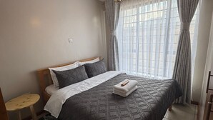 Een slaapkamer met een bed, een klein rond tafeltje, een tapijt met zebraprint en een plafondlamp.