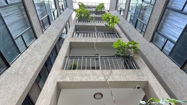 Een meerlaags gebouw met een centrale trap, grote ramen en balkons met beplanting.