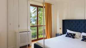 A bedroom with a large bed, a view of trees through a window, and a white radiator. - Raphael Stresa (Stresa)