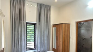 A bedroom with a bed, a wardrobe, a window with curtains, and a shower area.