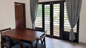 A room with a wooden dining table, chairs, and a view through a door with curtains.