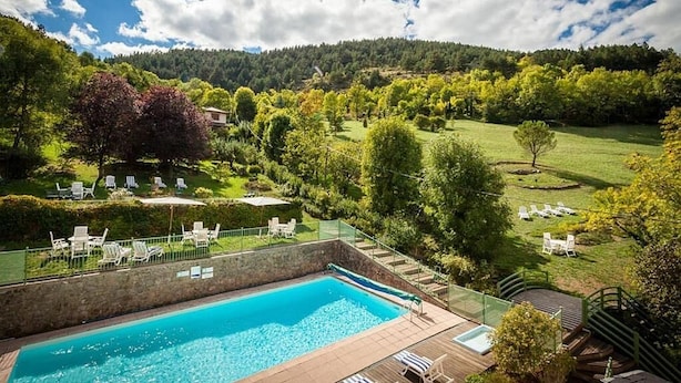 A swimming pool with lounge chairs and a view of a green landscape with trees and hills.