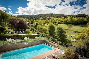 Piscina com espreguiçadeiras e vista para uma paisagem verde com árvores e colinas.