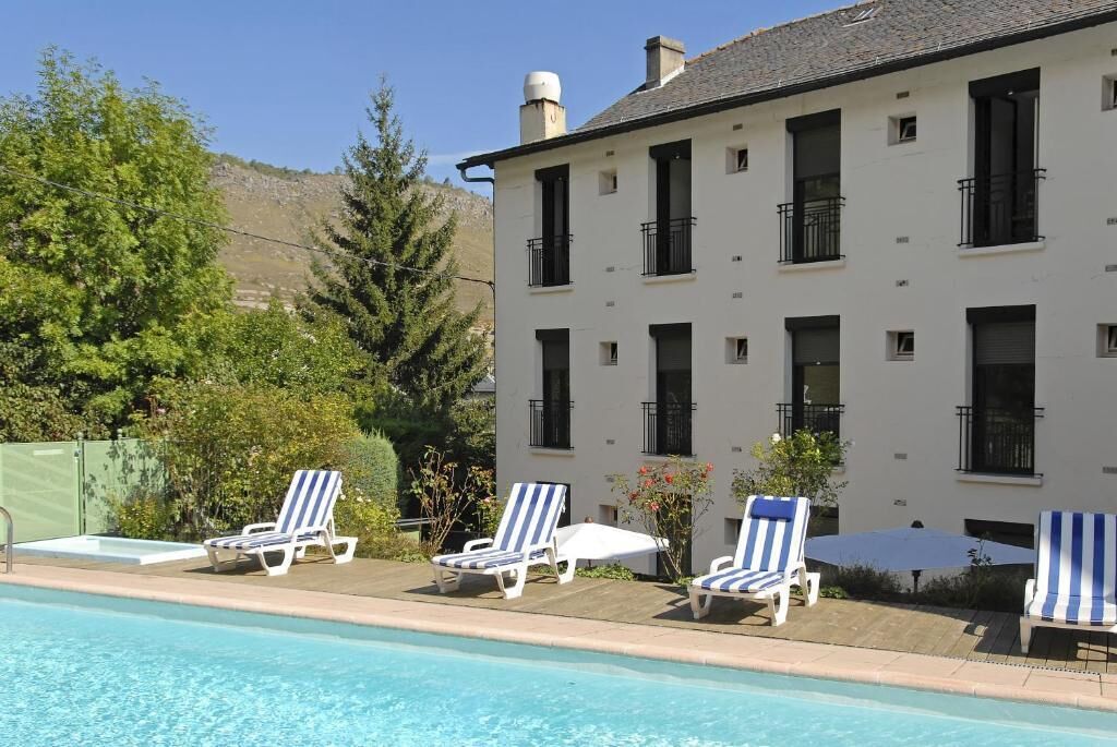 A building with a pool, surrounded by trees and a mountain.
