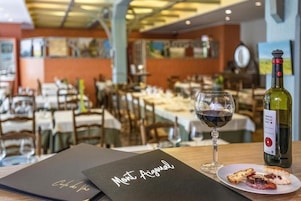 Interior de restaurante com mesas montadas para refeições, uma garrafa de vinho e um menu na mesa.