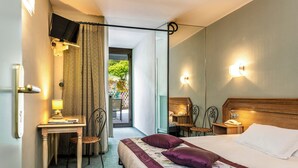A hotel room with a bed, a desk, a chair, a telephone, and a television.