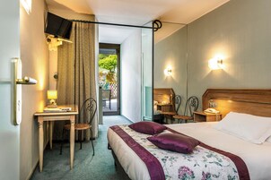 Quarto de hotel com cama, escrivaninha, cadeira, telefone e televisão.
