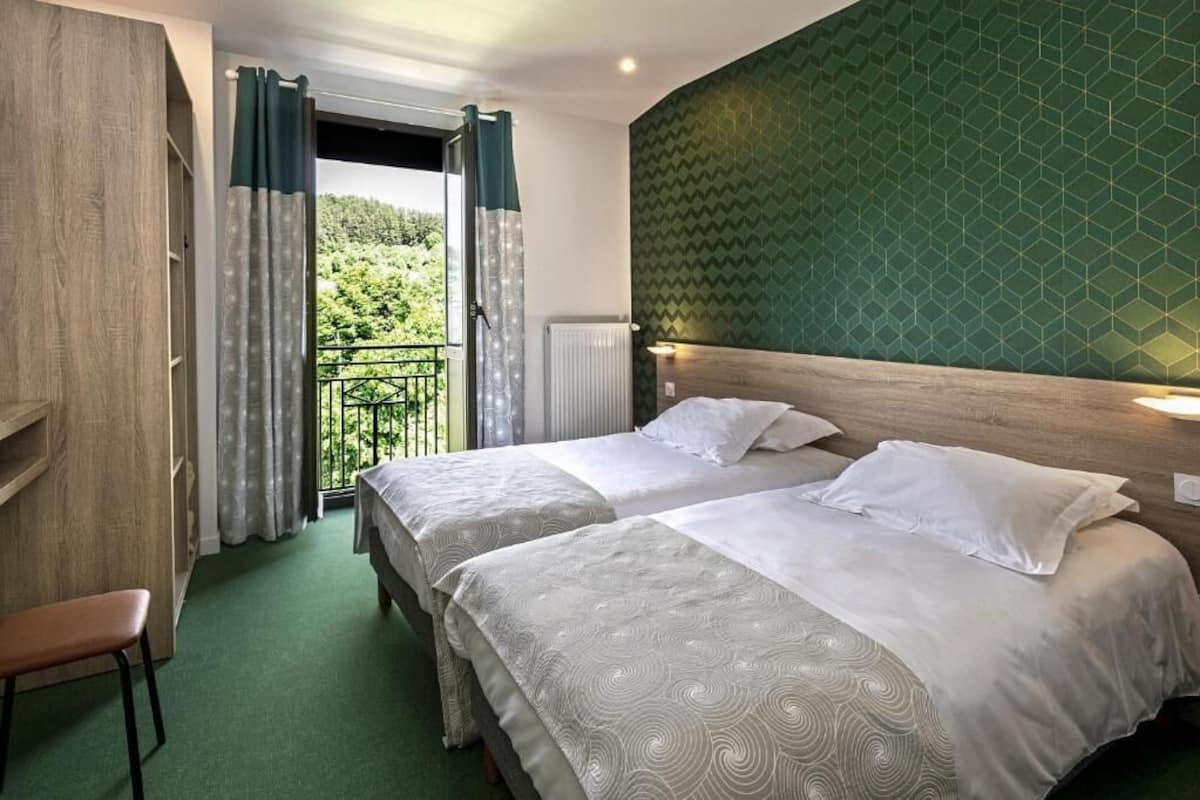 Une chambre d’hôtel avec deux lits, une armoire en bois, une chaise et un balcon avec des rideaux.