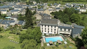 An aerial view of a residential area with a large building featuring a swimming pool, surrounded by greenery and other houses.