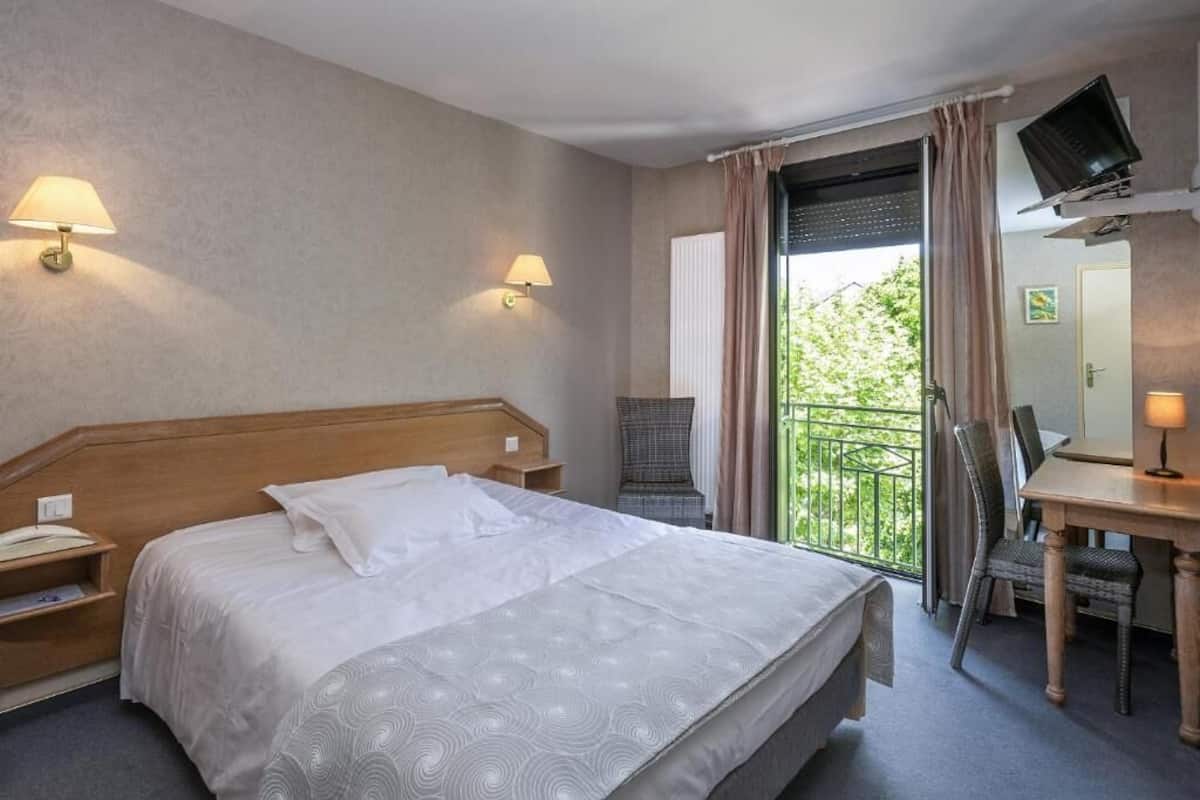 Une chambre d’hôtel avec un grand lit, un bureau avec une chaise, une télévision et un balcon avec des rideaux.