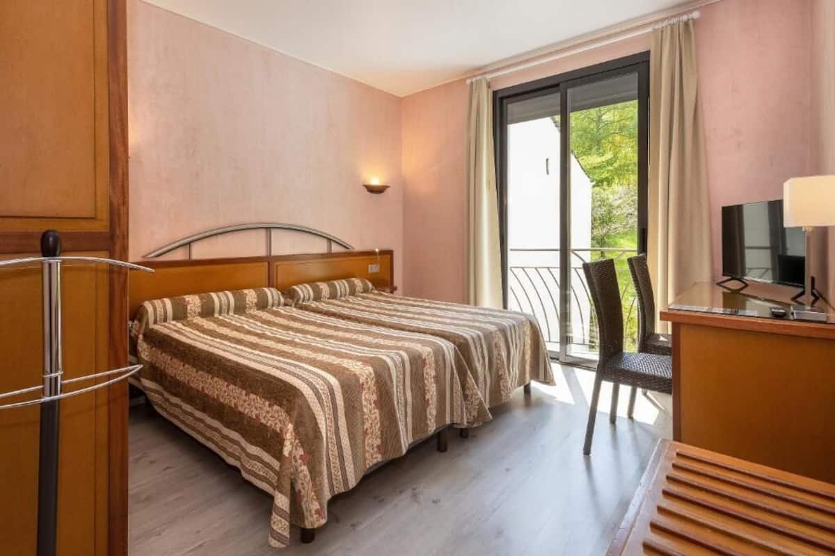 Une chambre d’hôtel comprenant un lit, un bureau avec une chaise, une télévision et un balcon avec une chaise.