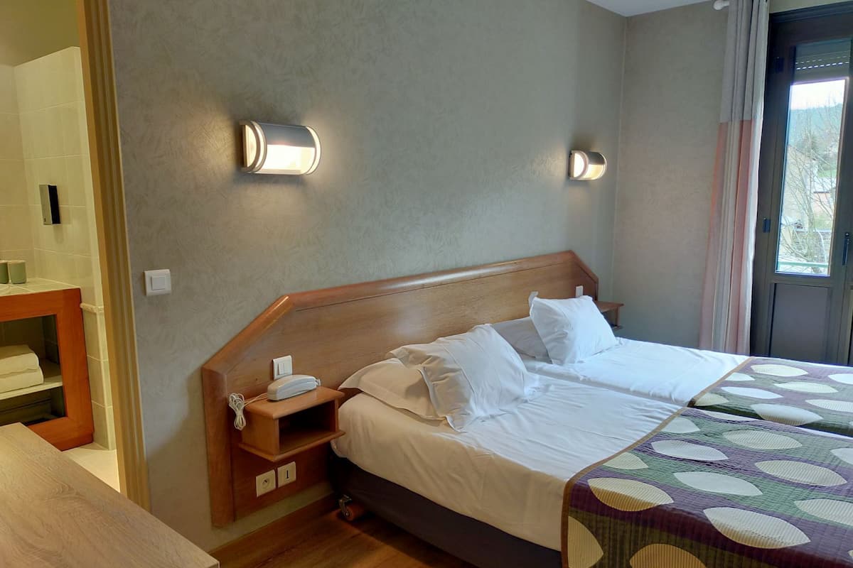 Une chambre d’hôtel avec une tête de lit en bois, un lit avec du linge de lit blanc, une table de chevet avec un téléphone et une petite table de nuit.