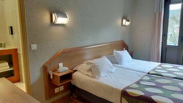 Una habitación de hotel con cabecera de madera, una cama con ropa blanca, una mesita de noche con teléfono y otra mesita de noche.