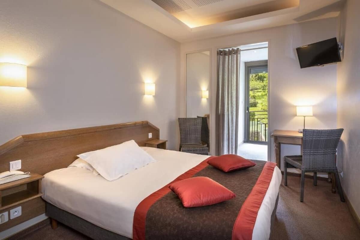Une chambre d’hôtel comprenant un lit, des tables de chevet, un bureau, une chaise, une télévision et un balcon avec des rideaux.