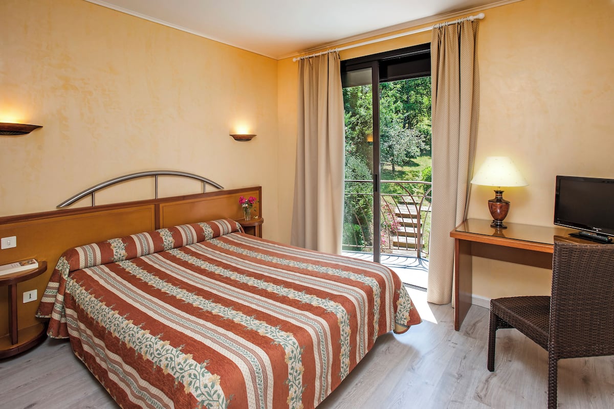 Une chambre d’hôtel avec un lit, un bureau avec une télévision, une chaise et une vue sur la verdure par la fenêtre.
