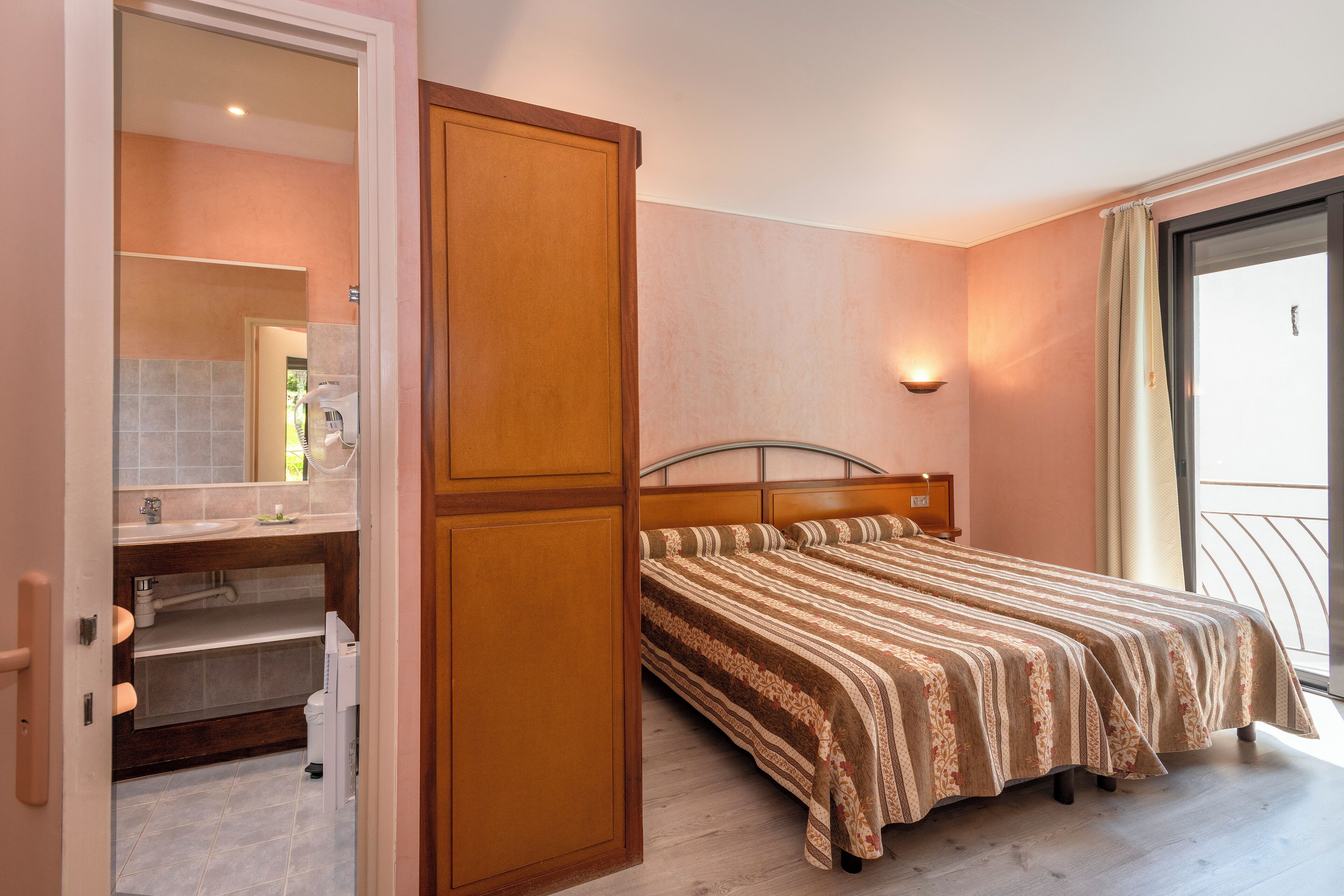Une chambre avec un lit, une salle de bain avec un lavabo et un miroir, et un balcon avec une balustrade.