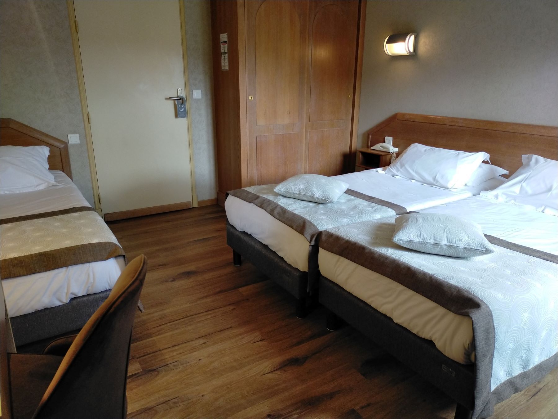 A hotel room with two beds, wooden flooring, and a wooden wardrobe.
