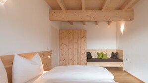 A bedroom with a wooden ceiling, a bed with white bedding, a wooden wardrobe, and a built-in bench with cushions. - Apartment Kardonighof Mareit (Kaltern)