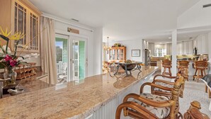 A spacious kitchen with a large island, wooden cabinets, and a dining area with wicker chairs. - Apollo Sunset: Elevator (Corolla)