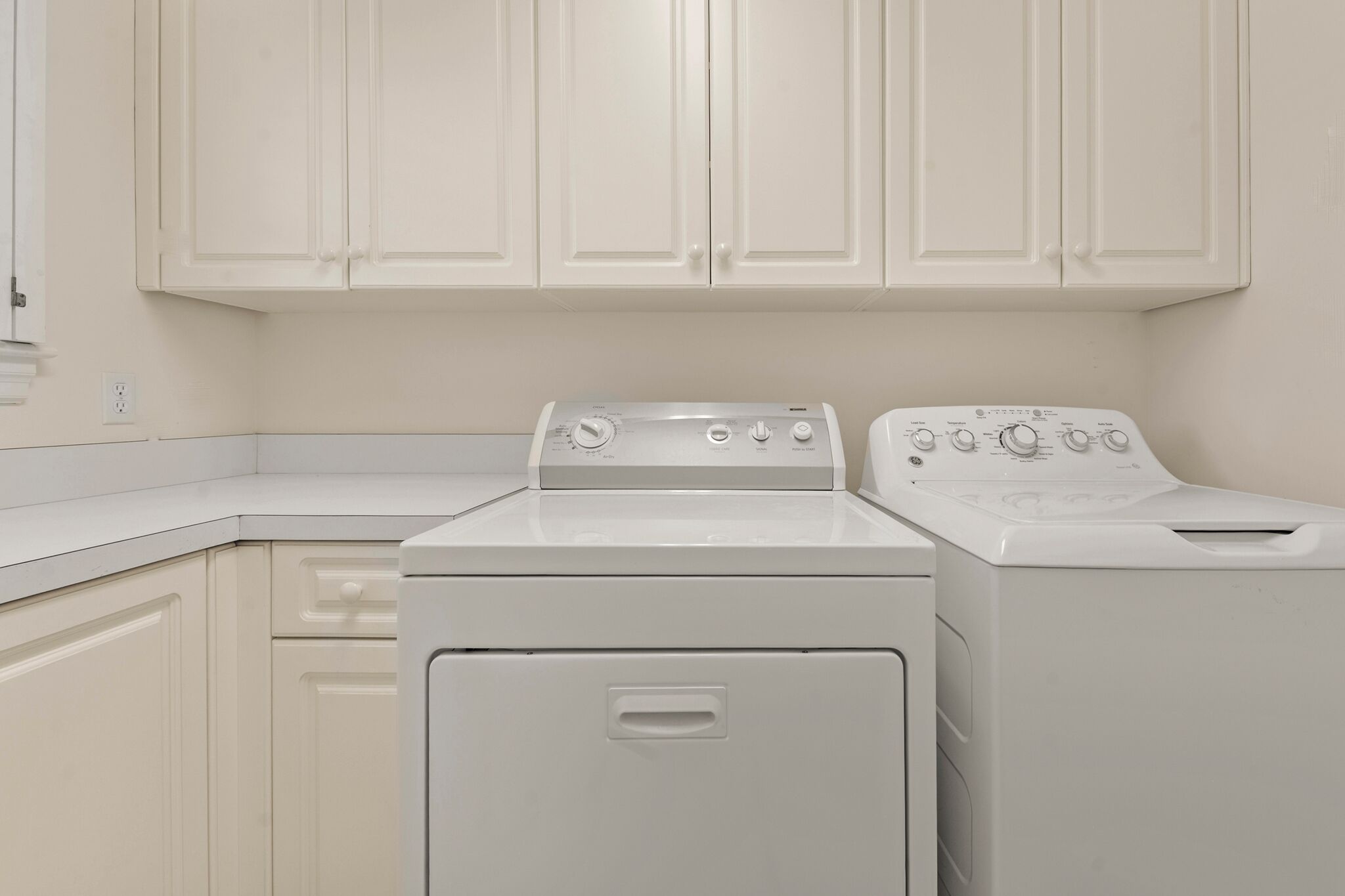 A laundry room with two white appliances, a dryer and a washer, and white cabinetry.