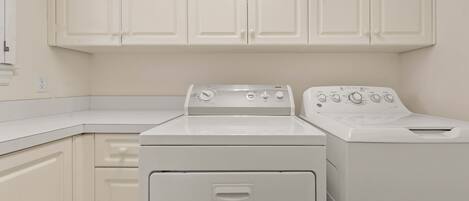 A laundry room with two white appliances, a dryer and a washer, and white cabinetry.