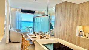 A modern hotel room with a balcony, a dining area, and a view of the sea.