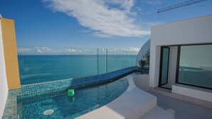 A modern infinity pool with a clear view of the ocean, a glass barrier, and a minimalist architectural design.