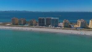 An aerial view of a coastal hotel complex with multiple high-rise buildings, a beach, and a clear view of the ocean.