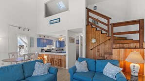 Ein geräumiger Wohnbereich mit einem blauen Sofagarnitur, einer Holztreppe und einer Küche im Hintergrund.
