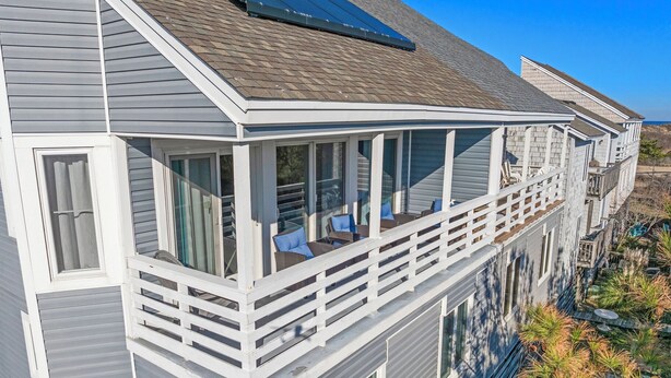Ein Haus mit überdachter Veranda, großen Fenstern und Solaranlage auf dem Dach.