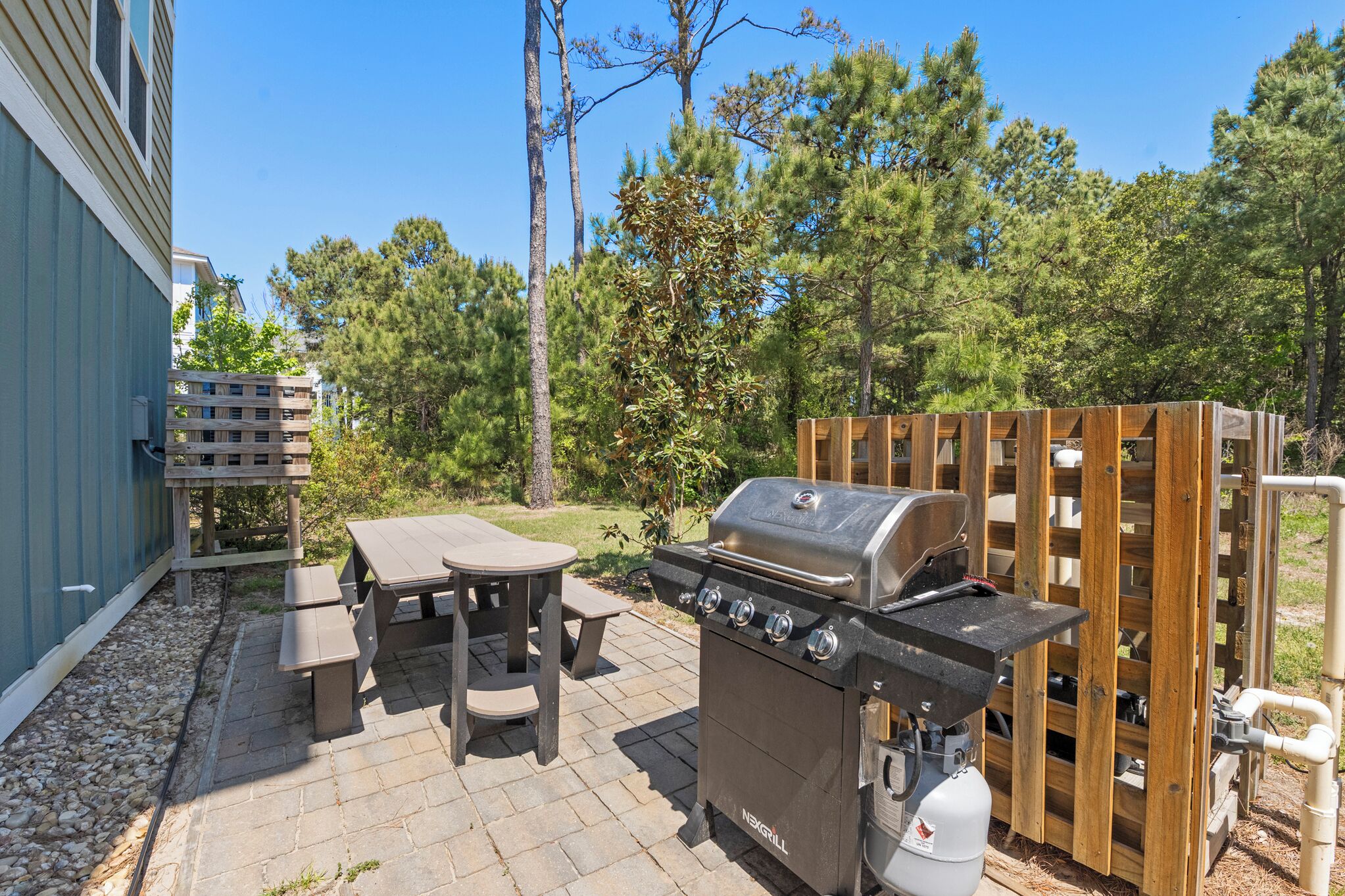 Un patio al aire libre con una parrilla, mesa de picnic y valla de madera.
