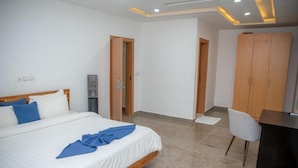 A modern hotel room with a large bed, a desk, and a wardrobe.
