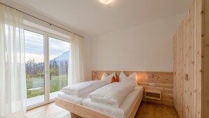 Une chambre à coucher avec un lit, des murs en bois, une vue à travers une porte vitrée et une table de chevet.