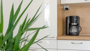 Une cuisine moderne avec une machine à café posée sur une étagère en bois, une plante en pot et des meubles de cuisine blancs.