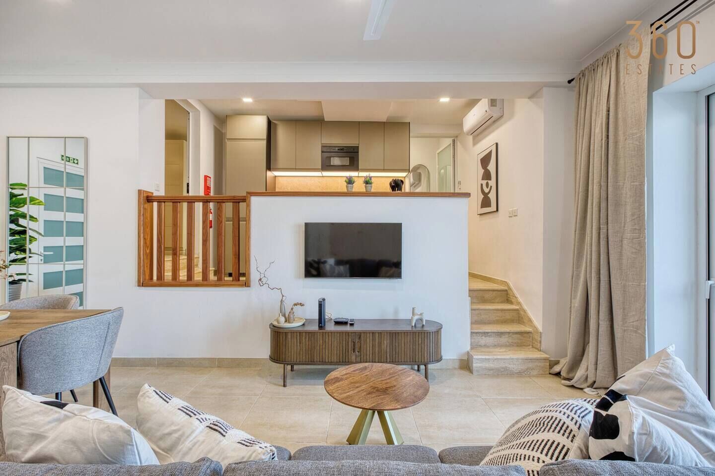 Un salon moderne comprenant un canapé, une table basse, un téléviseur et un escalier menant à la cuisine.