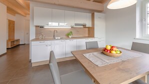 Moderni keittiö, jossa on valkoiset kaapit, puinen ruokapöytä ja hedelmäkulho.