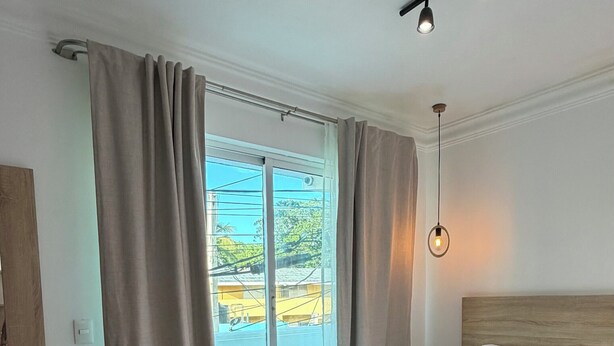 Een moderne slaapkamer met een groot bed, een glazen schuifdeur naar buiten en een plafondlamp.
