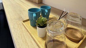 Een moderne keuken met houten keukenkastjes, een aanrecht en een dienblad met blauwe mokken, een klein plantje en glazen.