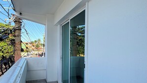Een balkon met betegelde vloer, een glazen deur en uitzicht op een straat met gebouwen en auto's.