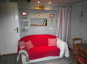 Ein Zimmer mit einem roten Sofa, einem Holzstuhl, einem Regal mit Zeitschriften und einer herzförmigen Dekoration.