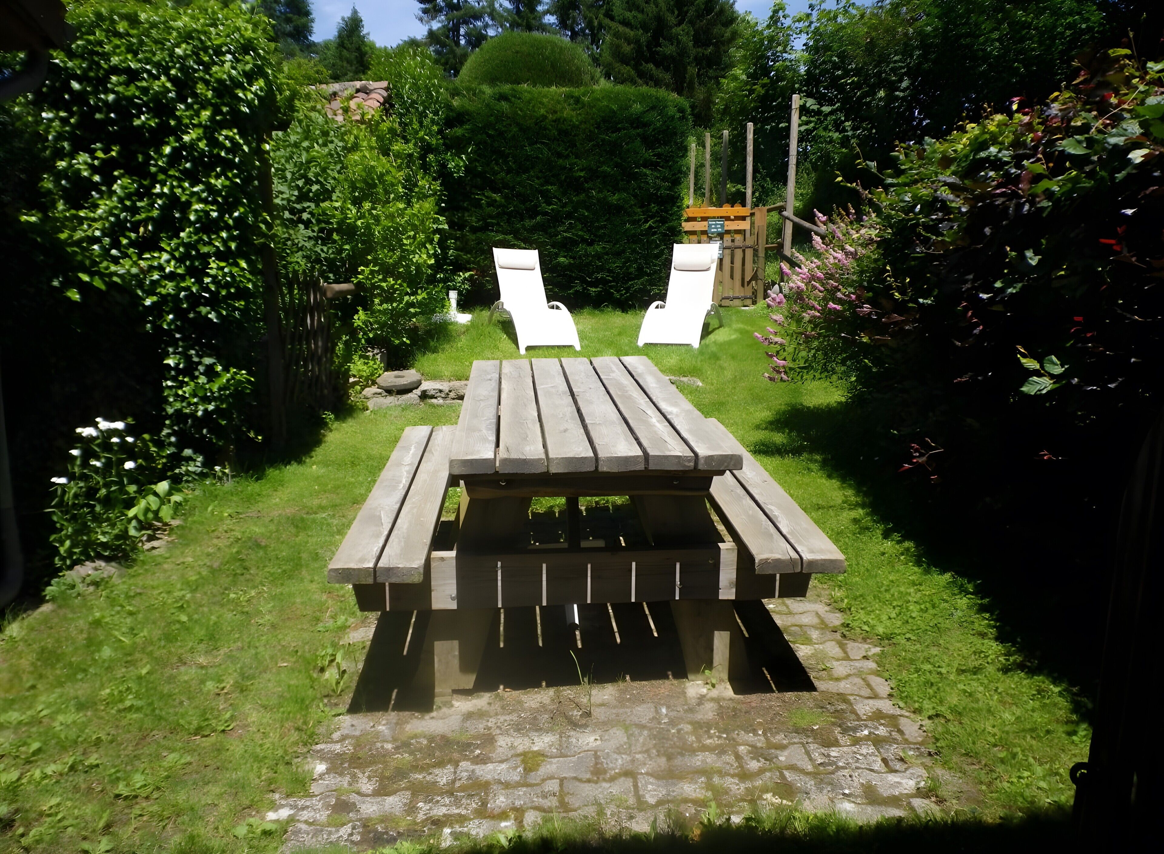 A wooden picnic table with benches in a garden with a stone pathway.