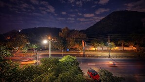 Een straatbeeld 's nachts, met een rode auto langs de kant, straatverlichting en een berg op de achtergrond.
